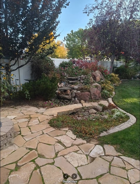 Backyard garden with flagstone pathway, colorful trees with autumn foliage, rock features, and lake view in background