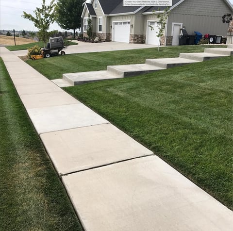 Concrete walkway and steps leading through manicured lawn toward a two-car garage house on a residential property