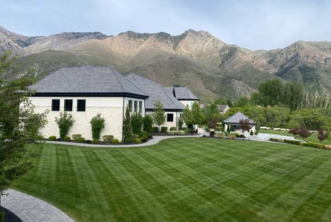 Modern white house with gray roof on manicured lawn backed by mountains