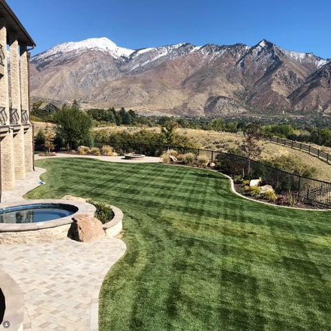 Luxury backyard with manicured lawn, hot tub, and stone patio overlooking snow-capped mountains