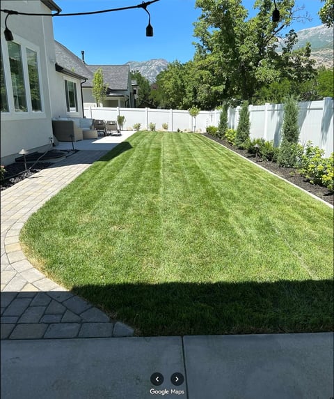 Manicured backyard with striped green lawn, white fence, paved patio, modern house, and mountains in background