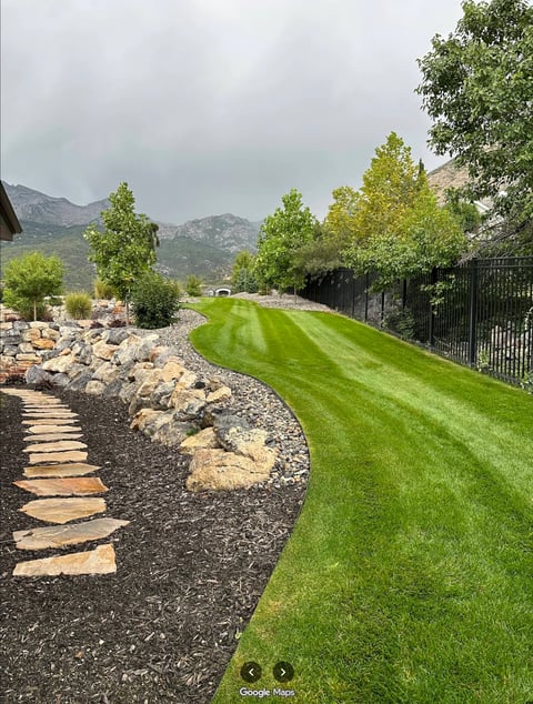 Landscaped backyard with manicured lawn, stone pathway, black fence, and mountain views in background