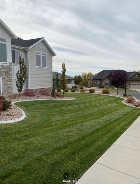Residential home with manicured lawn, landscaped garden beds, stone walkway, and mountain views in suburban neighborhood